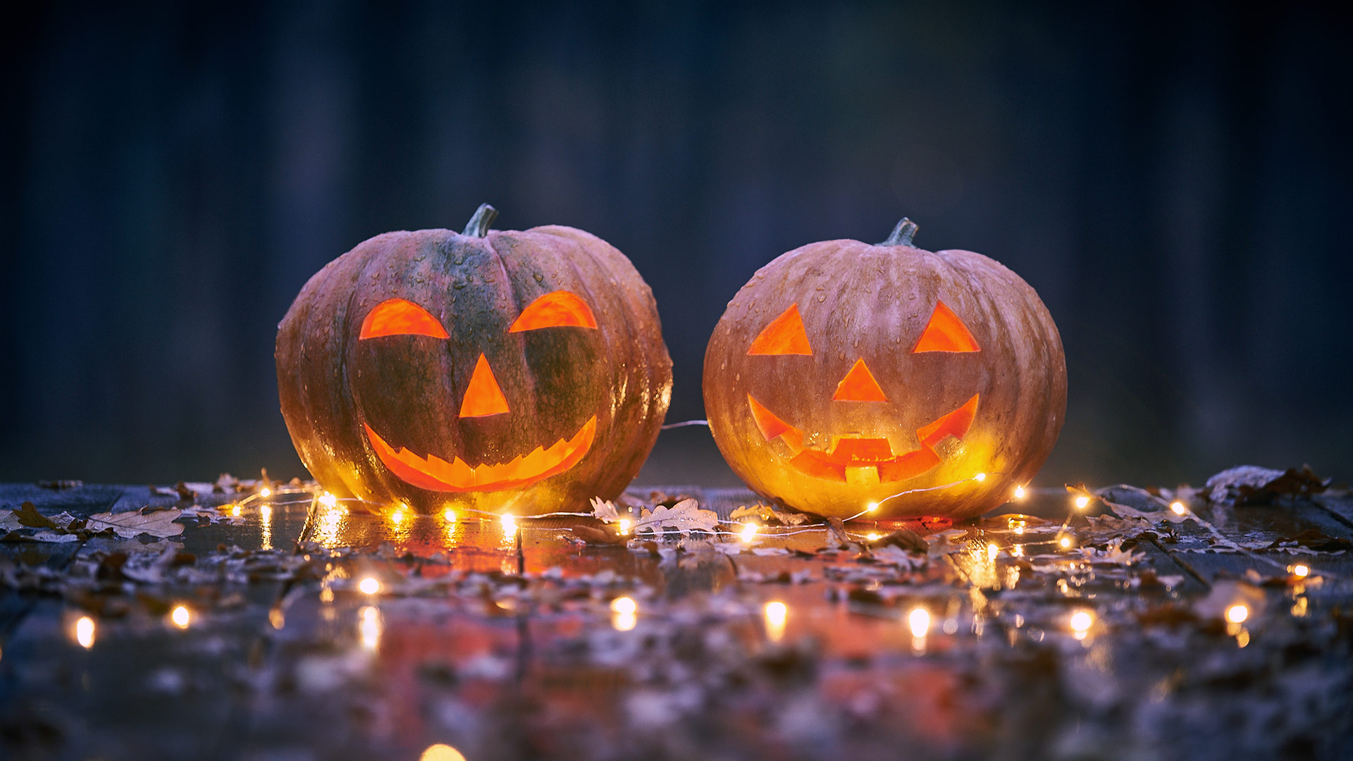 Two smiling Halloween pumpkins on a wooden table with lights In a mystic forest at night.
