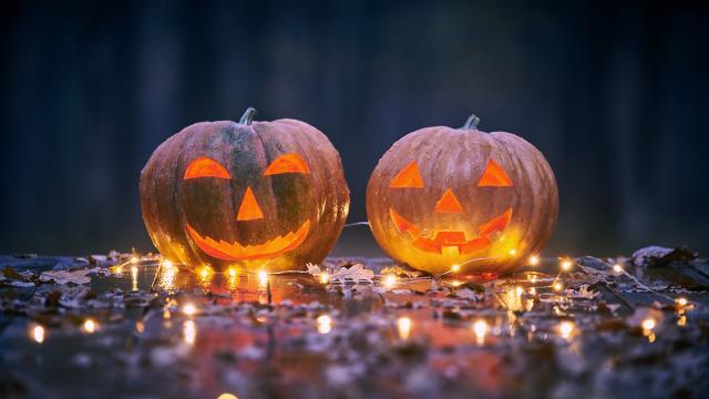 Two smiling Halloween pumpkins on a wooden table with lights In a mystic forest at night.